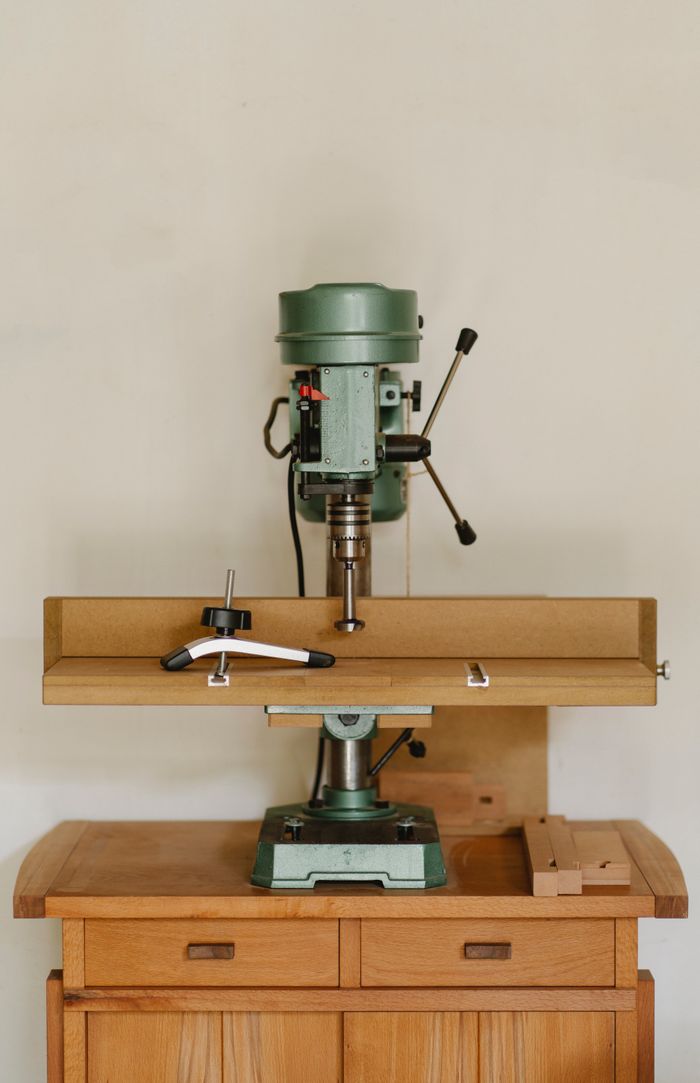 hero-02 Professional green metal drilling bench press for work with wood placed on wooden cabinet against white wall in carpentry workshop