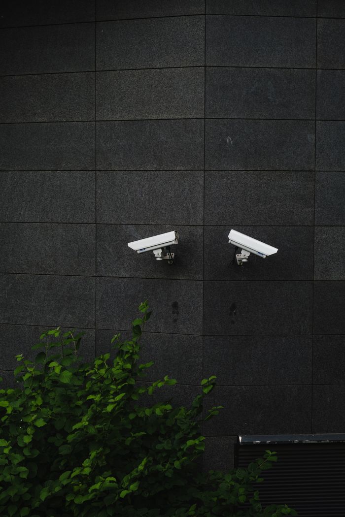hero-01 Two security cameras mounted on a dark tiled wall, symbolizing protection and surveillance.