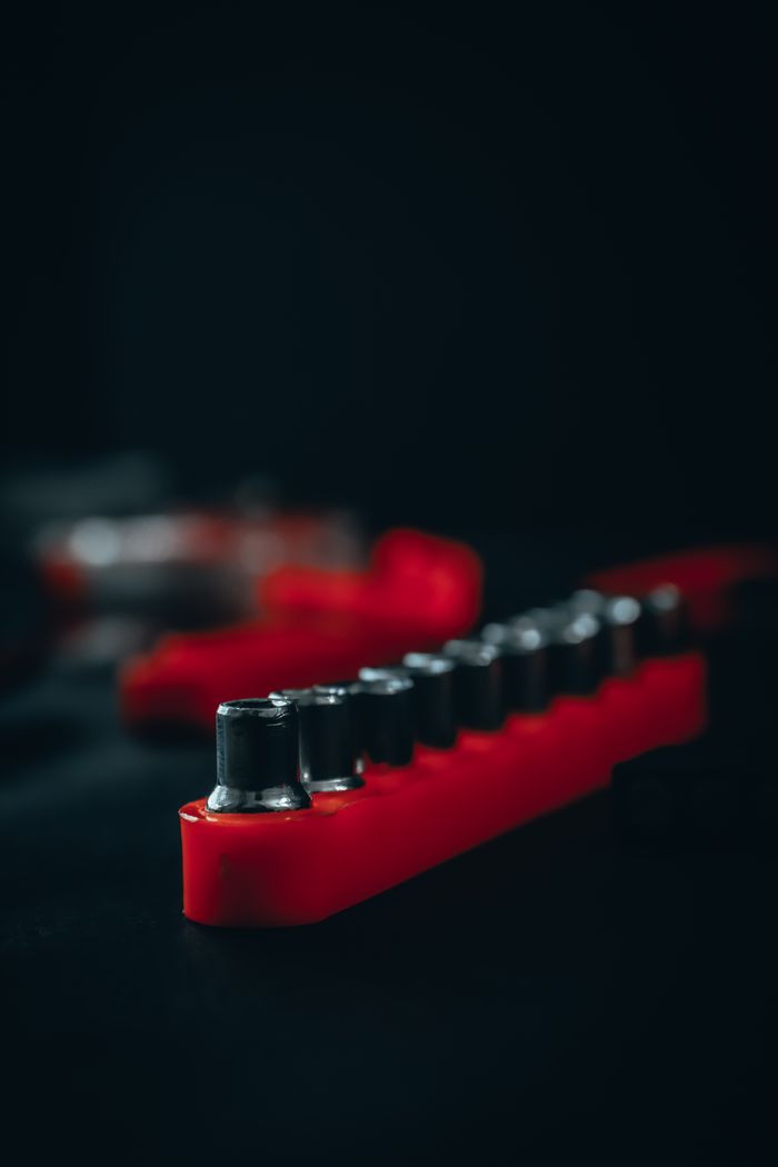 footer-02 Arrangement of metal drive sockets in red box placed on table near assorted service instruments in dark craftsmanship