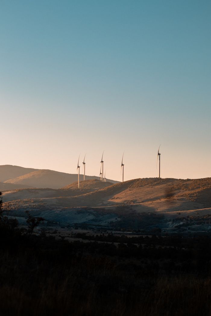 about-01 A serene landscape with wind turbines on rolling hills at sunset, showcasing renewable energy.